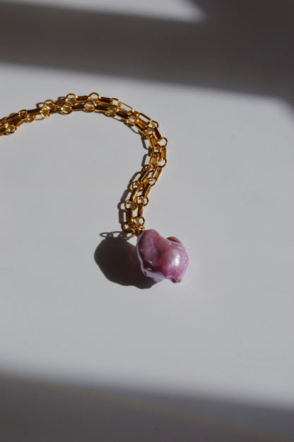 The Lavender Pearl Drop Necklace features a large, irregular pink freshwater pearl pendant on a 14k gold-filled chain, displayed on a white surface with subtle shadows.