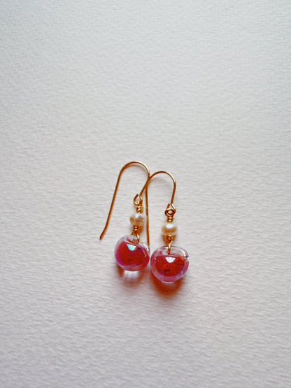 Bubble Minis: Gold hook earrings with round, translucent pink glass beads and small freshwater pearls displayed on a textured white surface.