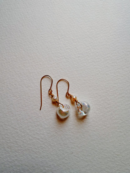 The Bubble Minis are delicate earrings with gold hooks, each featuring freshwater pearls and a round translucent glass bead, displayed on a textured white surface.