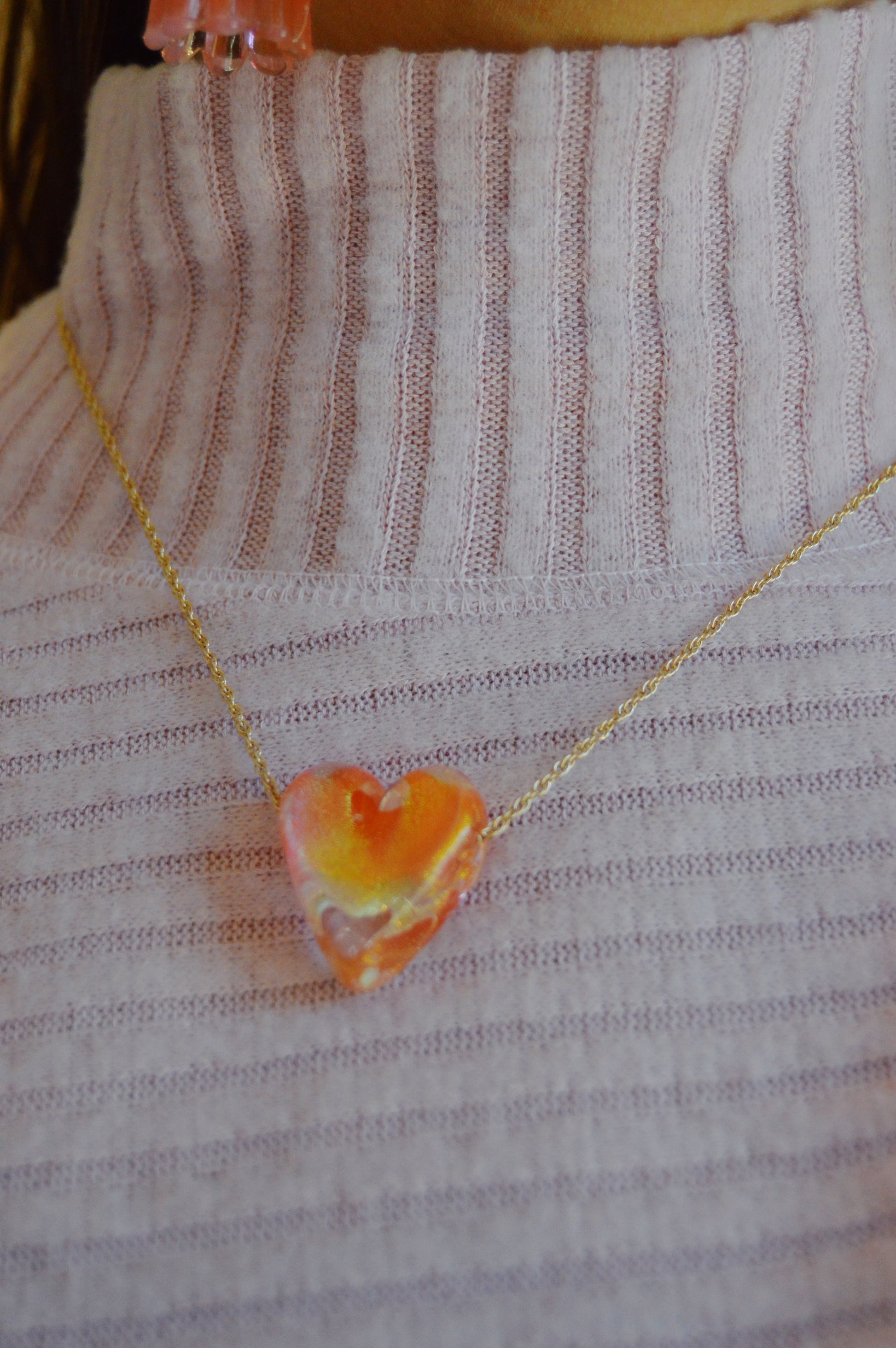 A person wearing a ribbed light purple turtleneck sweater and a gold-filled chain necklace featuring a handmade lampwork glass heart pendant from the Glass Heart Necklaces–Reds & Oranges collection.