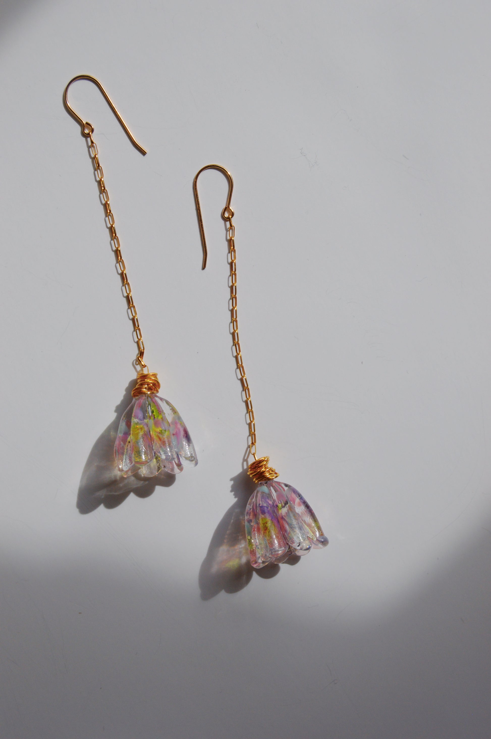 The Glass Tulips Earrings- Bloom are artisan-made gold chain drop earrings with translucent, flower-shaped pendants in pink, yellow, and green hues, beautifully displayed on a white surface with soft shadows.