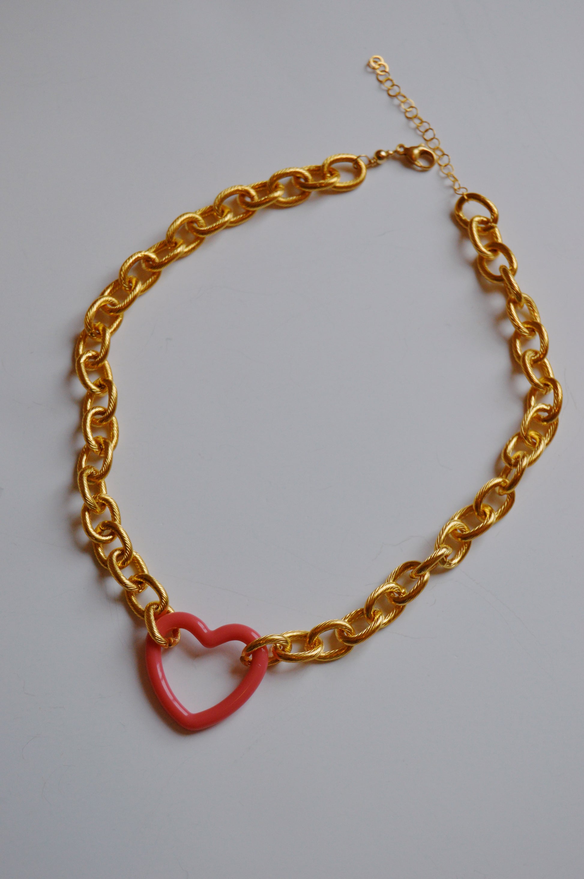 The Open Heart on Chunky Plated Chain showcases a pink acrylic heart charm on a gold-plated chain with large links, set against a simple light background—ideal for fans of handcrafted jewelry.