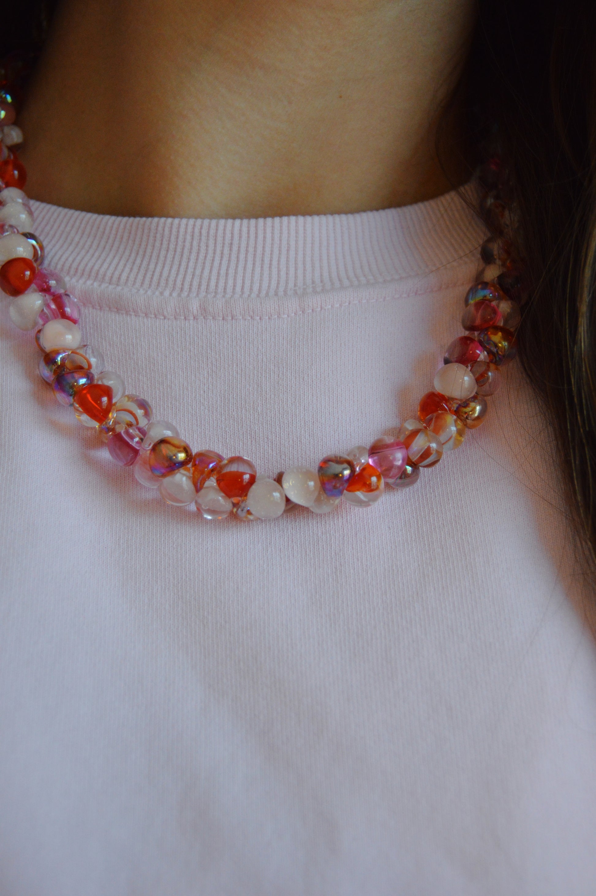 A close-up of a person wearing a white shirt and the Valentine Bubble Glass Necklace- Lovebug, featuring handmade red, pink, and multicolored round beads. The focus is on the necklace and upper chest area.