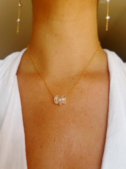 Wearing a Dainty Donut Layer 14K gold chain necklace with three clear round beads, the person in a white top also displays gold earrings accented with pearls and a subtle gold filled clasp.