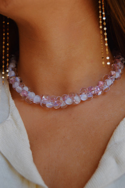 A close-up of a person wearing the Bubble Glass Necklace- Pink and Lavender with translucent pink and lavender beads, paired with gold-filled earrings and a white textured top.