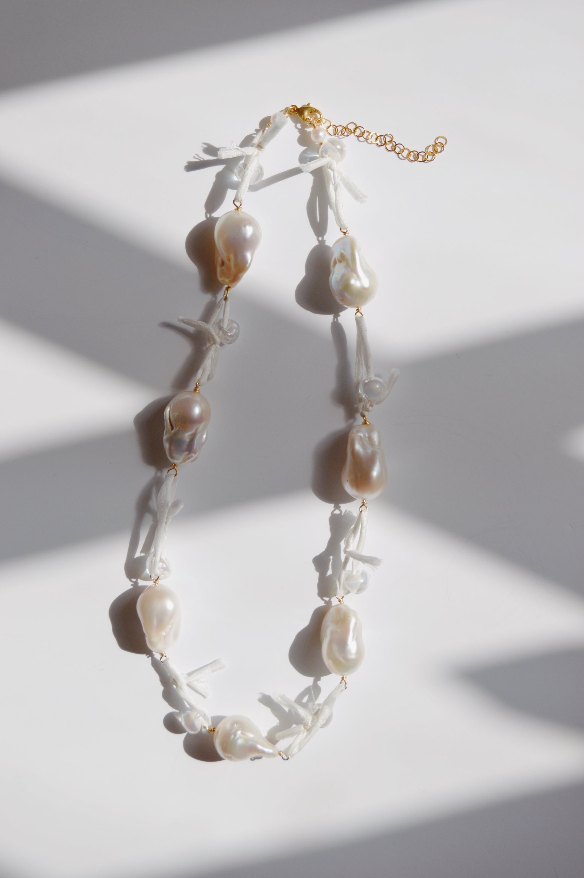 The Silk and Pearl Layer - White necklace features large, irregular white freshwater pearls with white silk knots between each pearl, displayed on a white surface with soft shadows—a unique piece of handmade jewelry.