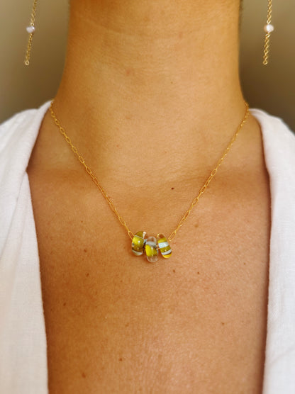 A close-up of a person wearing the Dainty Donut Layer—a 14K Gold Chain necklace with yellow, green, and white Glass Donut Beads. The person is in a white top against a neutral background.