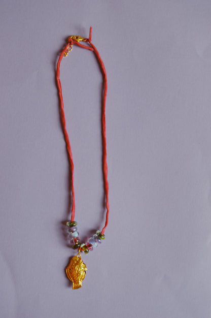 The Cloisonne Fish Layer - Berry features a red cord, handblown glass beads, and a 14k gold filled cloisonne fish pendant, shown on a light purple background.