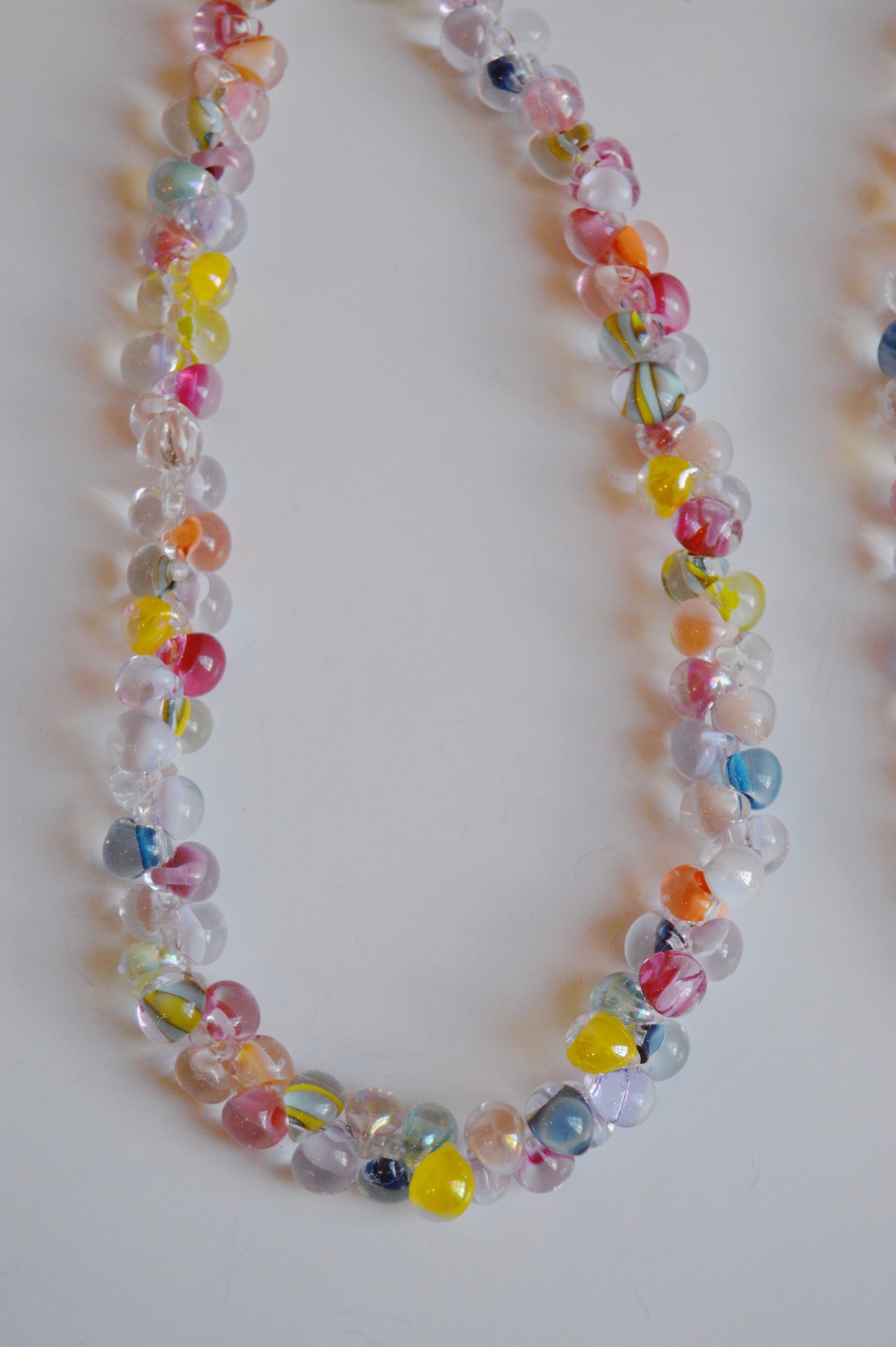 A close-up of the Rainbow Bubble Glass Necklace, showcasing handmade, colorful translucent round beads with vibrant swirls, artfully arranged in a loop on a white background.
