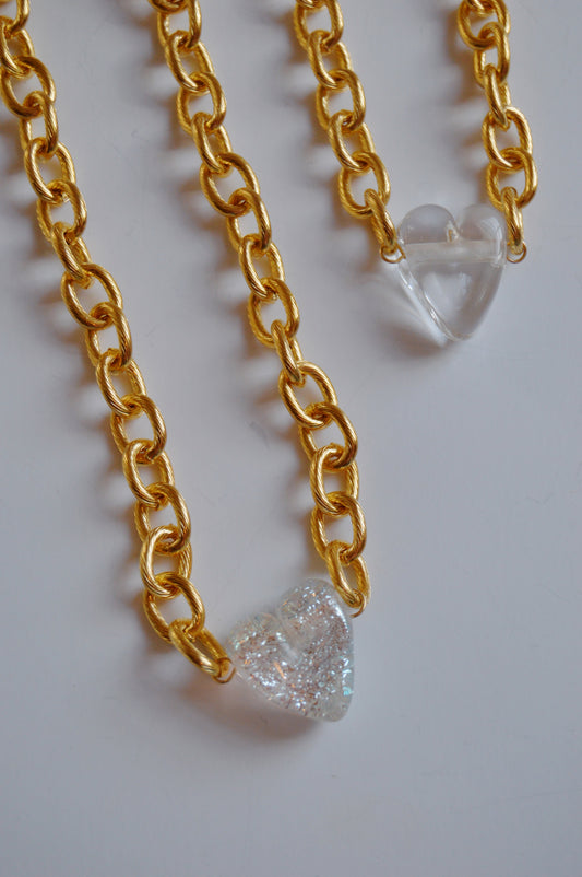 Two Chunky Plated Glass Heart Necklaces—Whites & Clears—rest side by side, each showcasing a unique handmade glass heart: one smooth and clear, the other glittery and textured for an artisan jewelry statement.