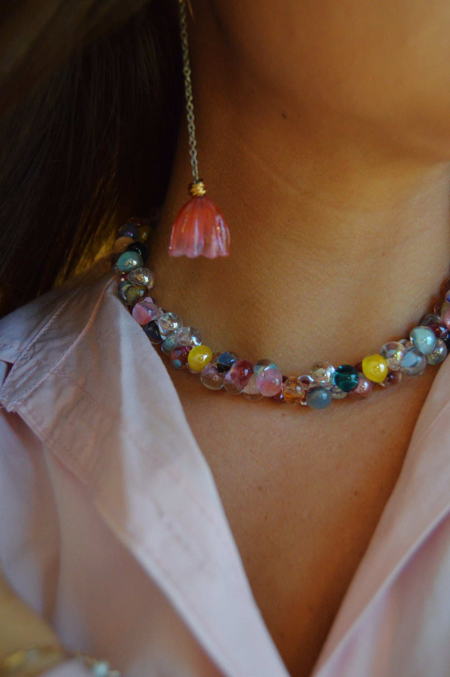 Close-up of a person wearing a pastel pink shirt and the Valentine Mix Bubble Glass Necklace, along with a dangling pink flower-shaped earring. The photo highlights the necklace and neck area, with the face partially out of frame.