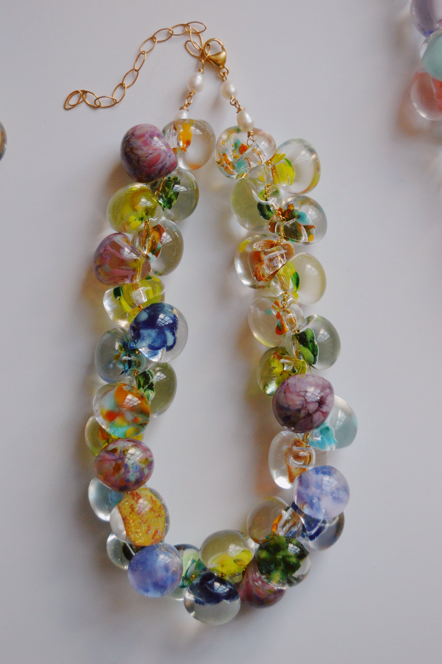 The Grand Bubble Necklace- Garden Mix is an artisan-made beaded necklace with handmade lampwork glass beads in vibrant floral patterns, finished with a gold clasp and adjustable chain, displayed on a white background.
