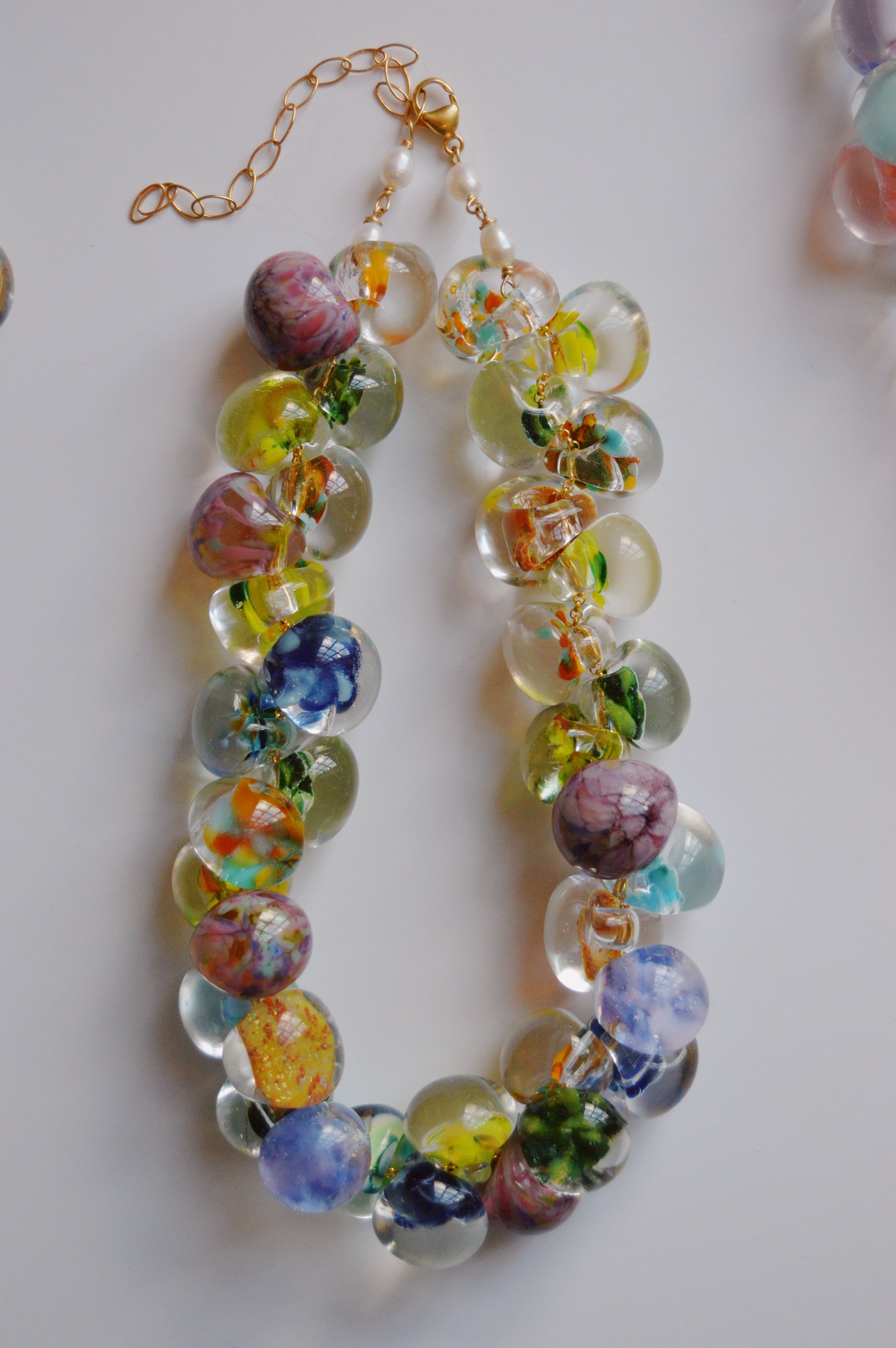 The Grand Bubble Necklace- Garden Mix is an artisan-made beaded necklace with handmade lampwork glass beads in vibrant floral patterns, finished with a gold clasp and adjustable chain, displayed on a white background.