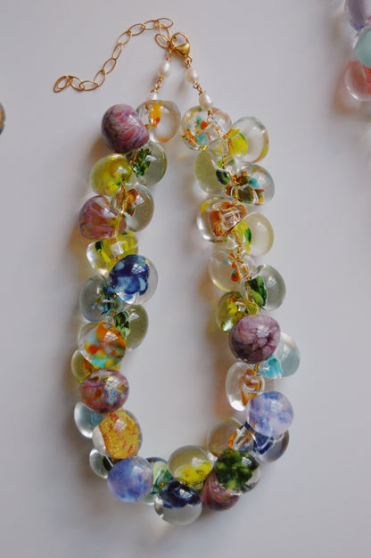 The Grand Bubble Necklace- Garden Mix is an artisan-made beaded necklace with handmade lampwork glass beads in vibrant floral patterns, finished with a gold clasp and adjustable chain, displayed on a white background.