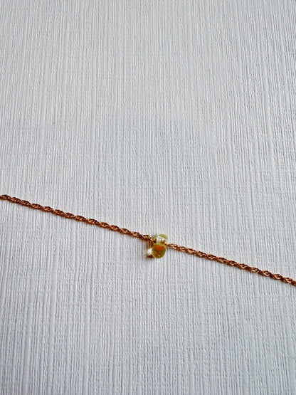 A delicate 14k gold filled Dewdrop Bracelet adorned with a small yellow gemstone, displayed on a textured white surface.