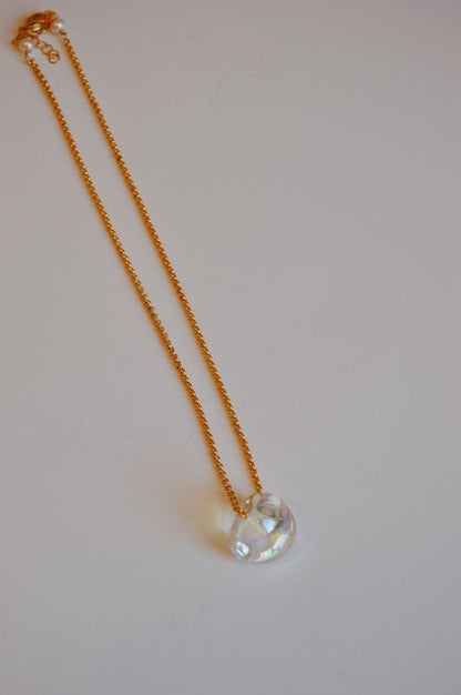 The Grand Bubble Single - Constellation features a gold filled chain necklace with a clear, iridescent glass pendant and delicate glass beads, displayed on a simple light surface.