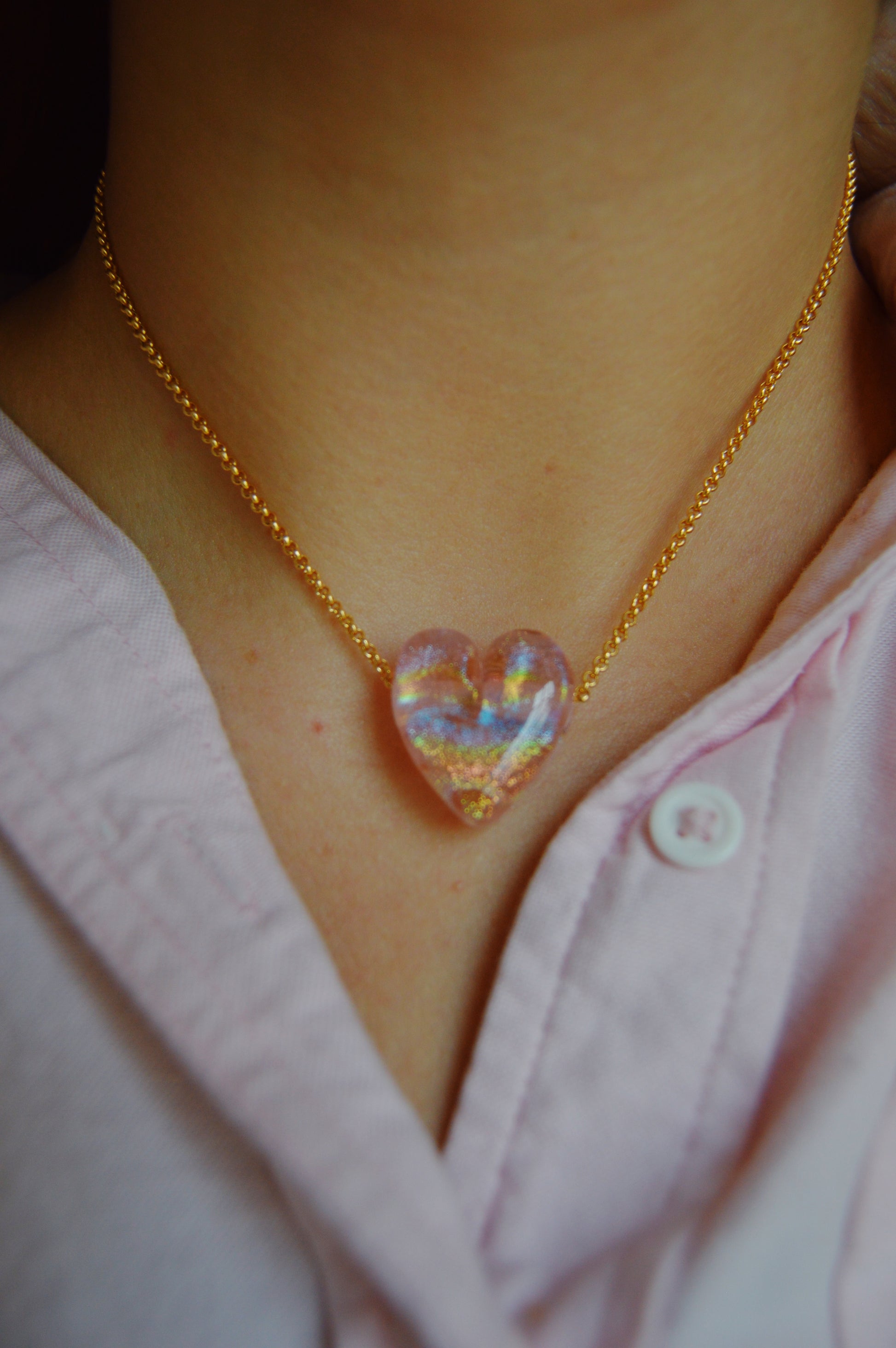A person wears a pink collared shirt and the Glass Heart Necklaces- Pinks: an artisan-made lampwork glass heart pendant on a 14k gold-filled chain.