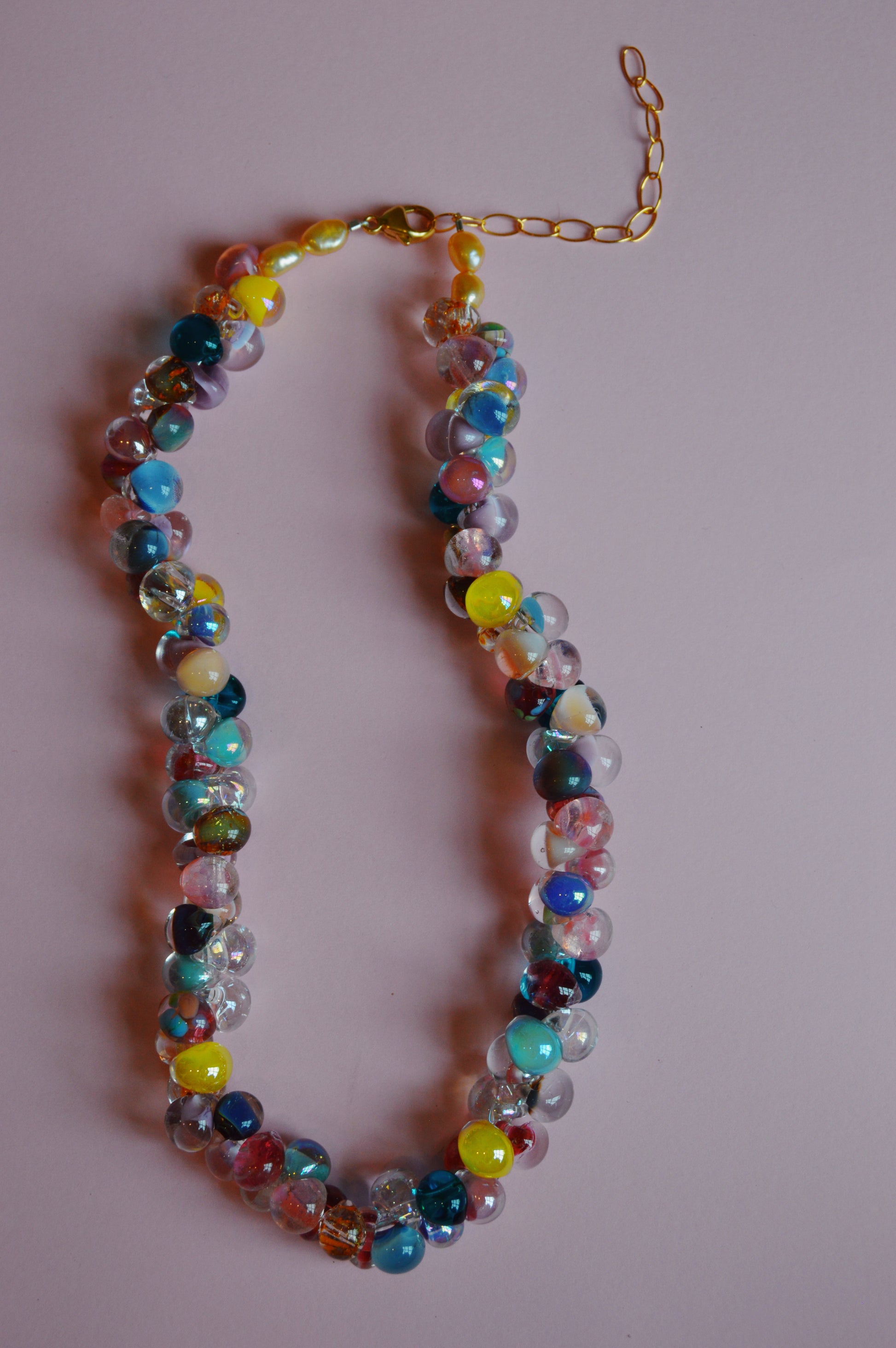 The Valentine Mix Bubble Glass Necklace features multicolored round beads and a gold chain clasp, displayed in a loose oval on a light pink background.