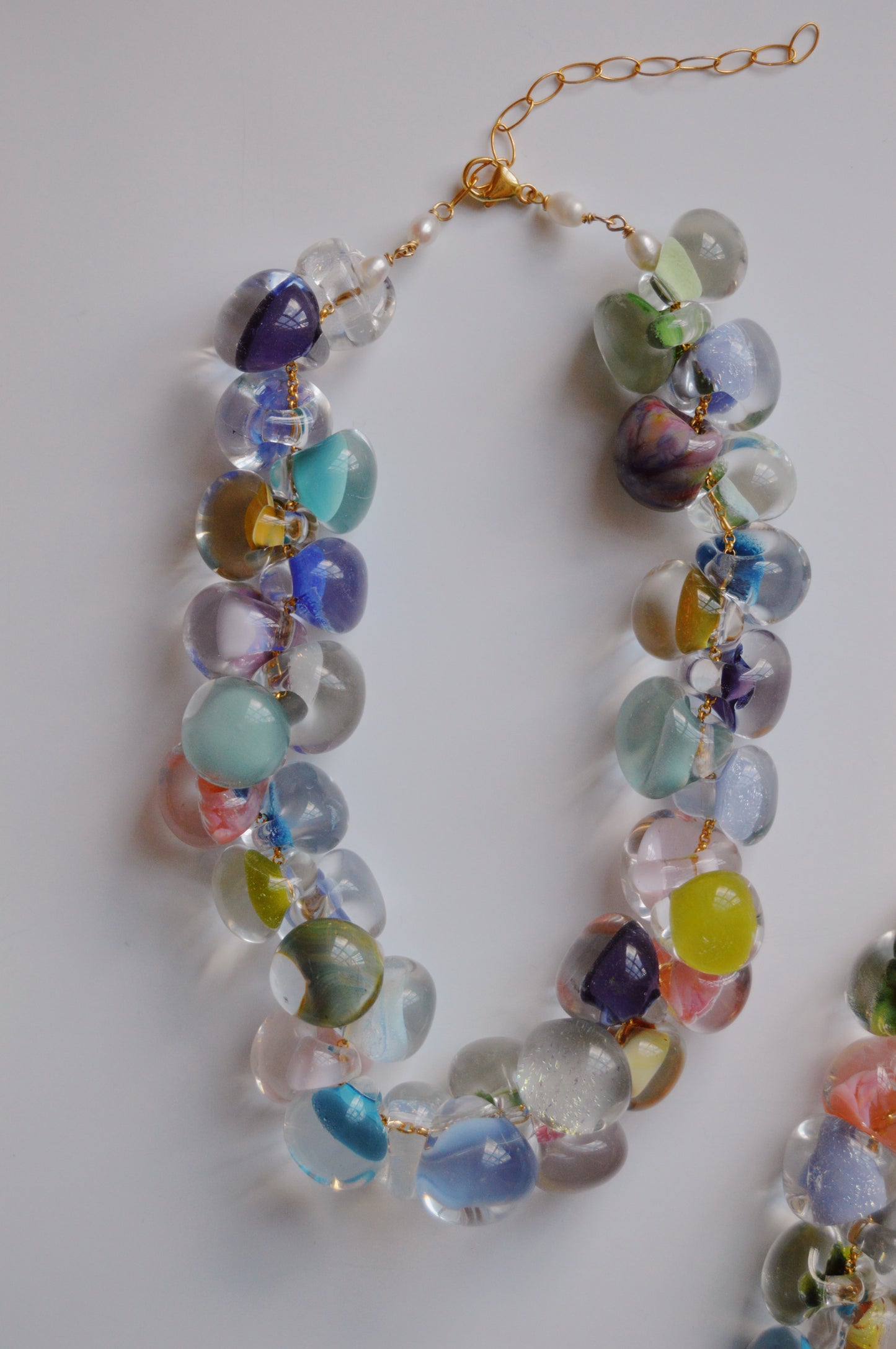 The Grand Bubble Glass Necklace- Cabana Mix showcases large, round handmade lampwork glass beads in vibrant blue, green, purple, pink, and yellow, linked by gold wire with 14k gold-filled findings on a white surface.
