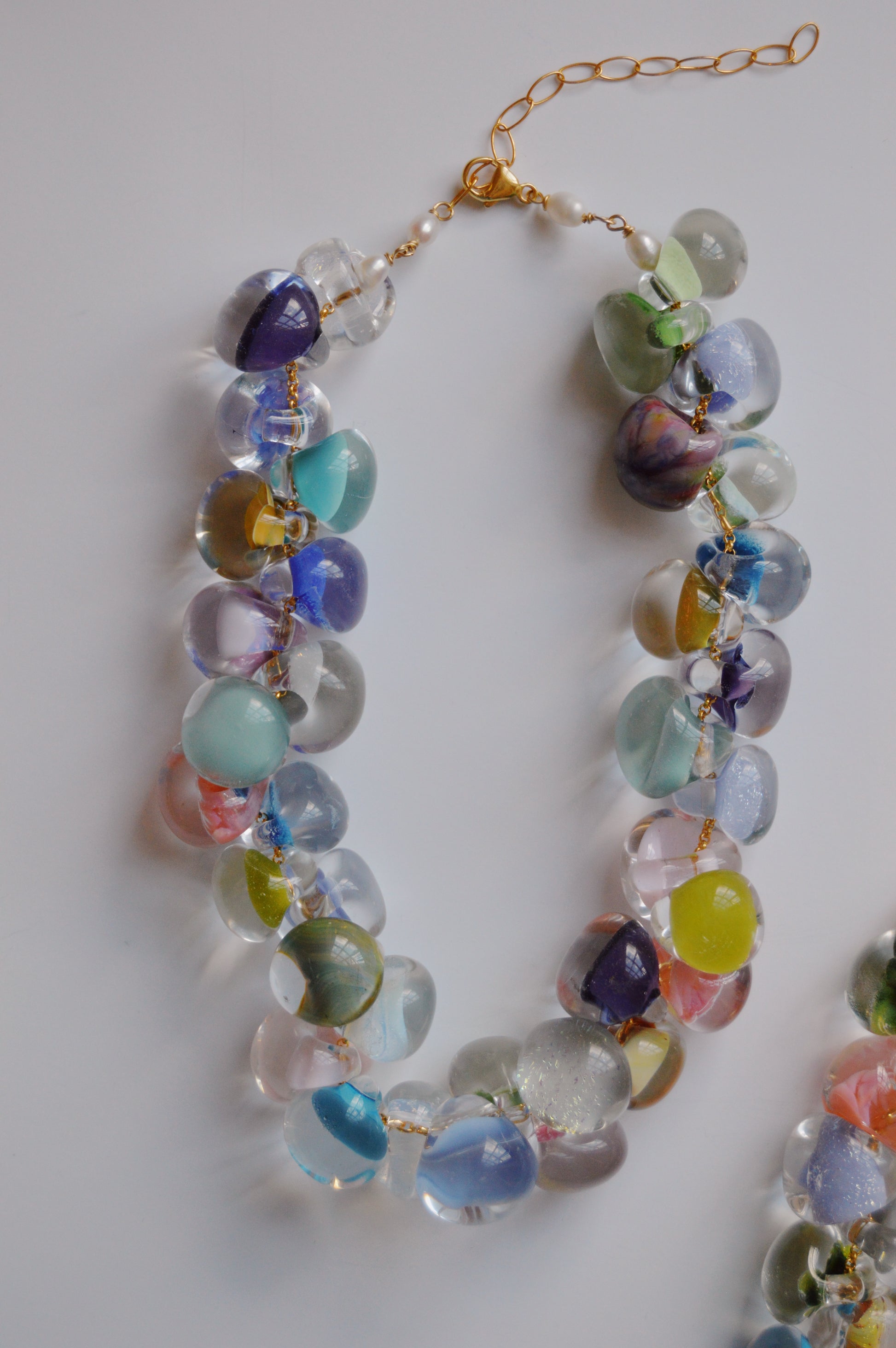 The Grand Bubble Glass Necklace- Cabana Mix showcases large, round handmade lampwork glass beads in vibrant blue, green, purple, pink, and yellow, linked by gold wire with 14k gold-filled findings on a white surface.