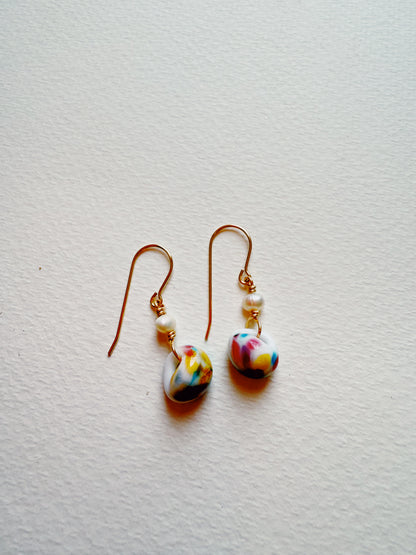 Bubble Minis: Dangle earrings with gold filled findings, each adorned with a small freshwater pearl and a round glass bead featuring colorful abstract patterns, displayed on a textured white surface.