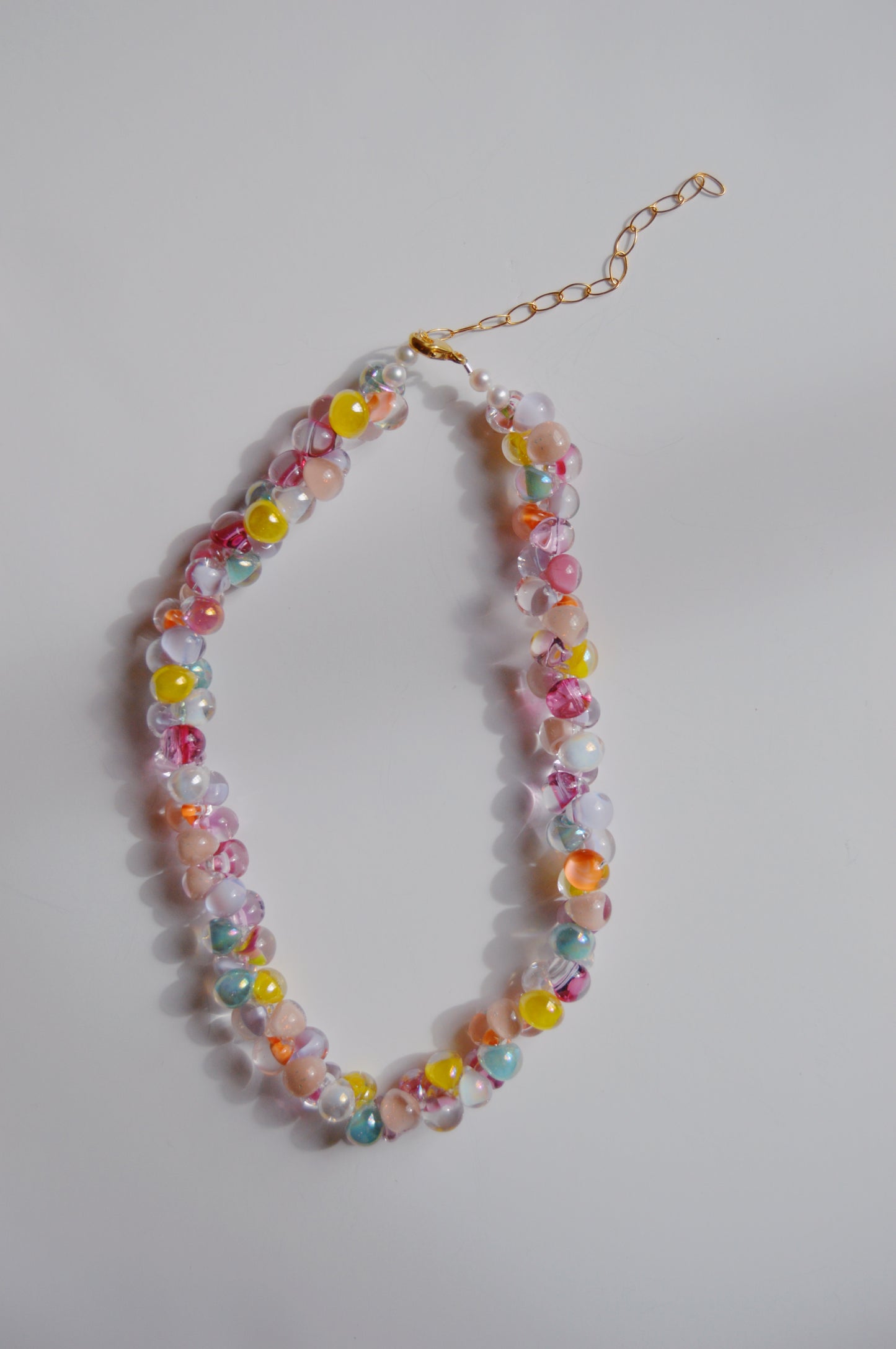 The Rainbow Bubble Glass Necklace in marshmallow features colorful round beads and cultured freshwater pearls, with a gold adjustable chain clasp, elegantly arranged in an oval on a plain white background.