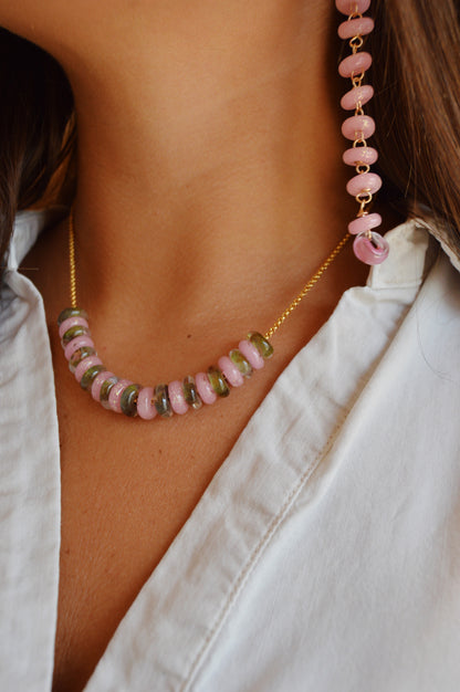 A close-up of a person wearing a white collared shirt and the Fall Lots of Donuts Layer—a necklace with pink and green handblown glass beads on a 14k gold filled chain. A matching beaded accessory appears near the shoulder.