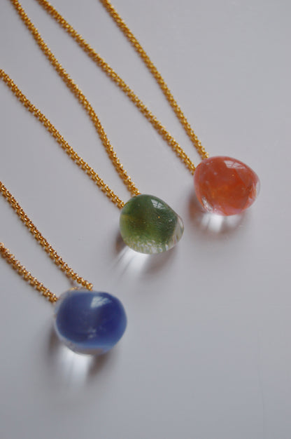 Three "Grand Bubble Single-Petal" gold-filled chain necklaces, each with a smooth, rounded handmade lampwork glass pendant in blue, green, and red, are arranged diagonally on a white background for a vibrant look.