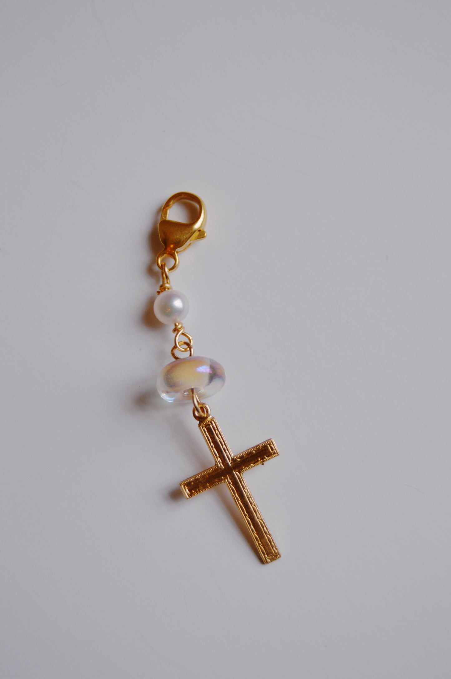 The Glass and Cross Charm keychain features a gold lobster clasp, a small white pearl, a clear handmade lampwork glass bead, and a 14k gold filled cross pendant. Shown on a plain white background.