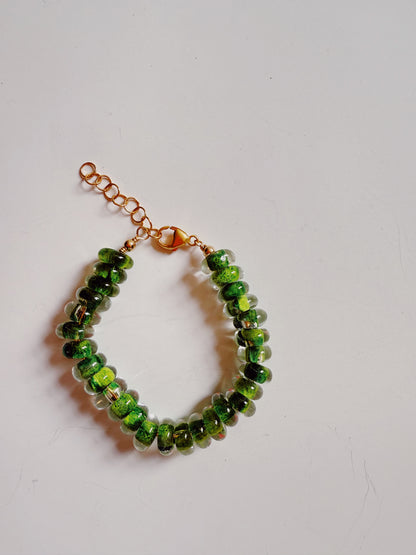 The Donut Bracelet features handblown green glass beads with gold accents on a 14k gold-filled chain and lobster clasp, displayed against a plain white background.