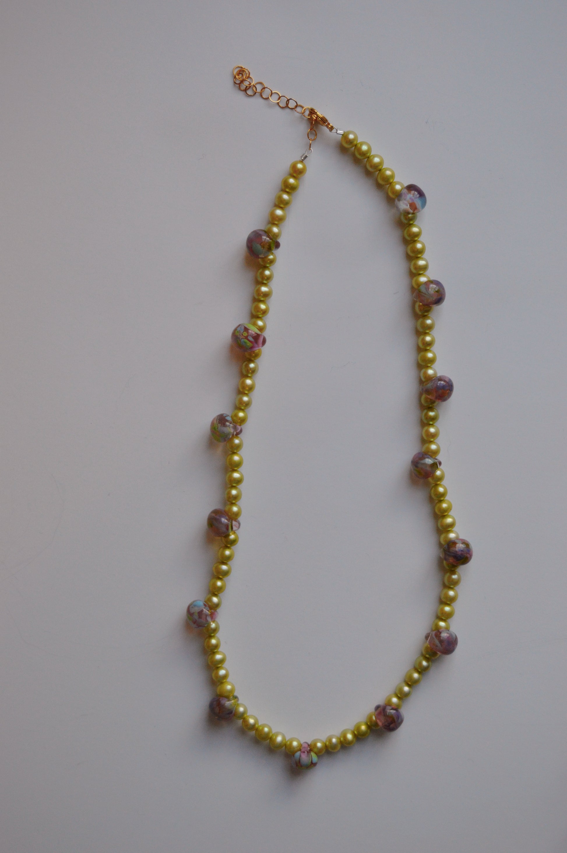 The Bubble and Pearl Layer necklace features small yellow beads, handmade floral lampwork glass beads, and larger round beads, all displayed on a plain white background.