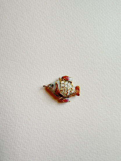 A Fish Anklet with gold, white, and red detailing rests on a textured, off-white surface.