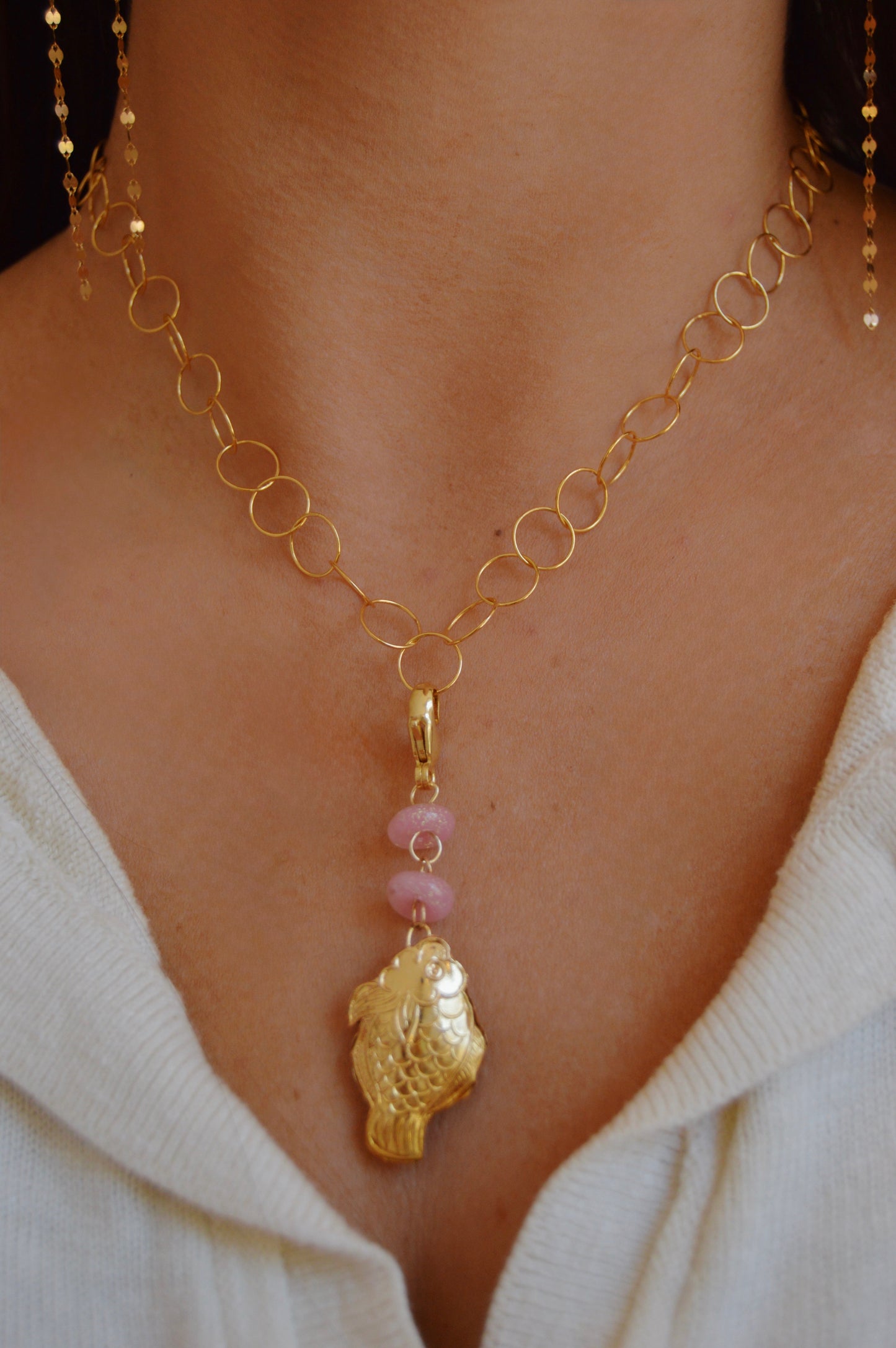 A woman wears the "Glass and Fish Charm": a 14k gold-filled oval link chain necklace with a Cloisonne Fish pendant and two pink handmade lampwork glass beads, styled over a light V-neck top.