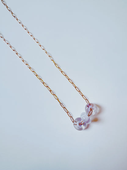 The Dainty Donut Layer is a delicate 14K gold chain necklace featuring three translucent round glass donut beads, shown on a plain white background.