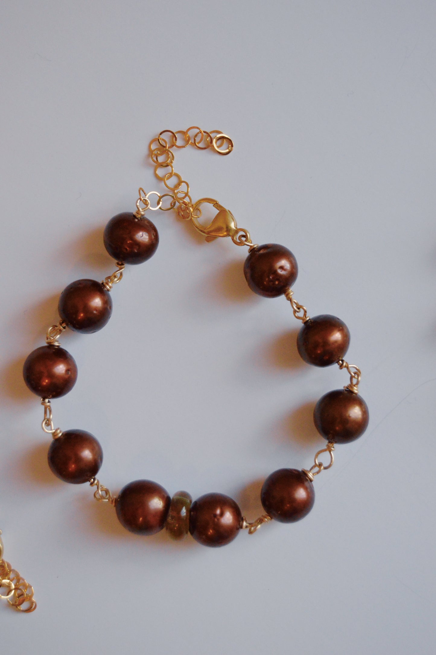 The Pearl and Glass Bracelet features large, round, brown handmade lampwork glass beads on a 14k gold-filled chain with a lobster clasp and adjustable extension, elegantly displayed on a light surface.