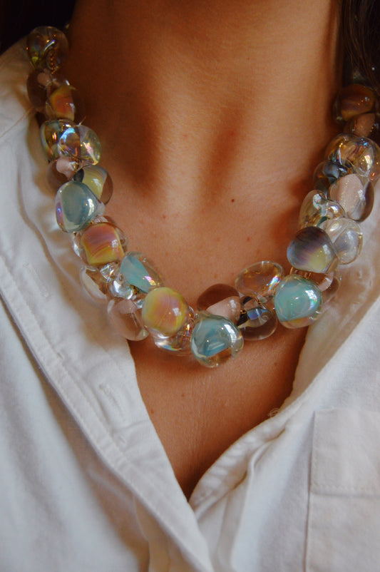 A person wears the Grand Bubble Necklace- Muted Mix, featuring large artisan-made lampwork glass beads, styled over a white collared shirt. The vibrant necklace draws attention to the neckline.