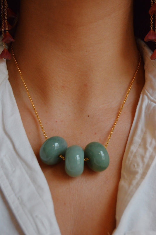 A close-up of a person wearing the Grand Donut Layer-Green necklace—featuring four large, smooth natural agate donut beads on a gold-filled chain—paired with a white collared shirt.