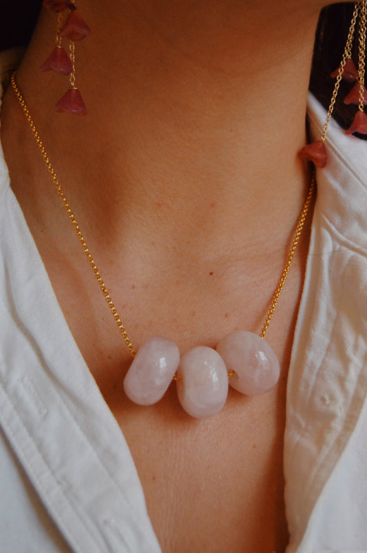 A close-up of a person wearing the handcrafted Grand Donut Layer-Pink gold-filled chain necklace with three large, smooth pale pink stones and matching earrings—an elegant statement paired with a crisp white shirt.