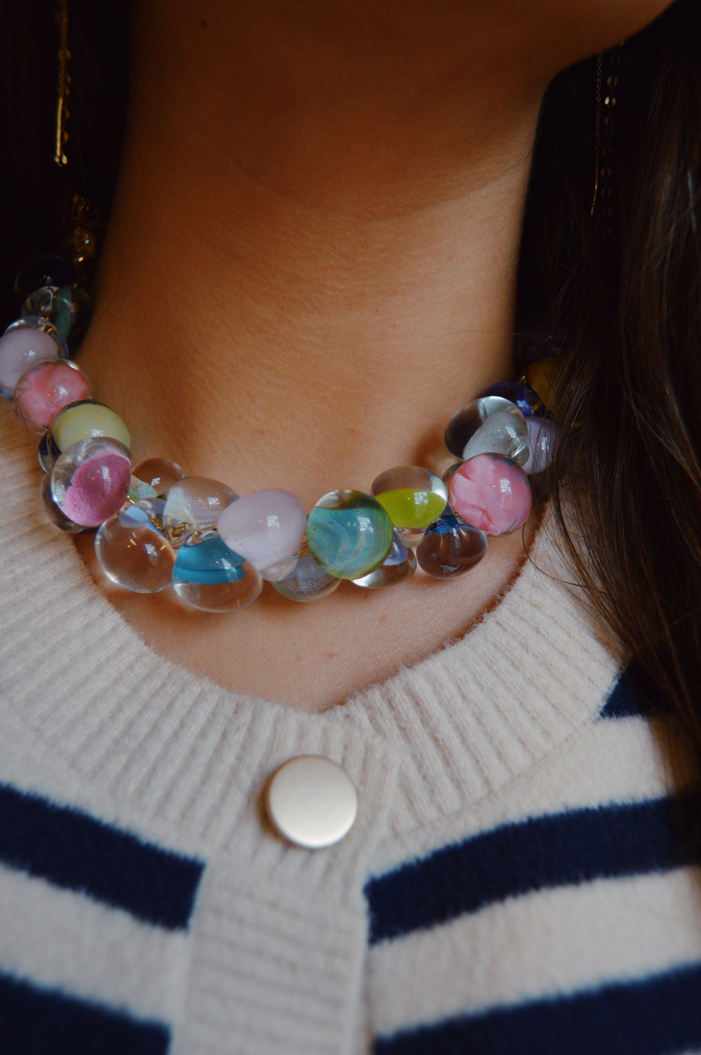 Close-up of a person wearing the Grand Bubble Glass Necklace- Cabana Mix, a chunky and colorful piece featuring handmade lampwork beads, paired with a cream and navy striped knit top accented by a round silver button.