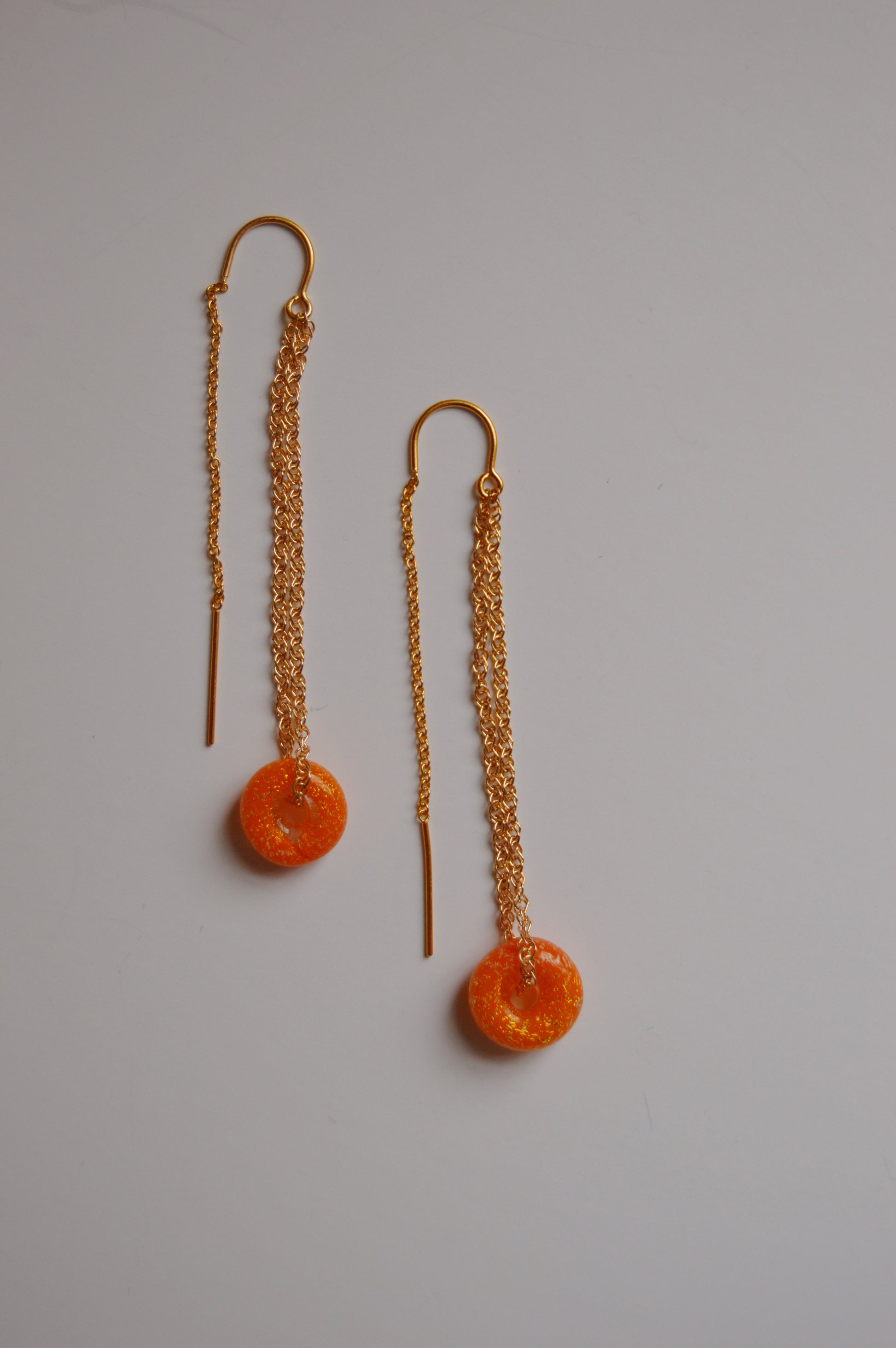 A pair of Donut Threaders- Sunshine Sparkle earrings featuring gold chains, orange handmade lampwork glass beads, and straight gold bars, displayed on a plain white background.