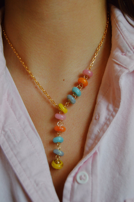 A person wears a pink collared shirt and a gold-filled chain necklace—the Donut Lariat- Sparkle Mix—with handcrafted, colorful round lampwork glass beads in yellow, pink, blue, orange, and purple arranged vertically.
