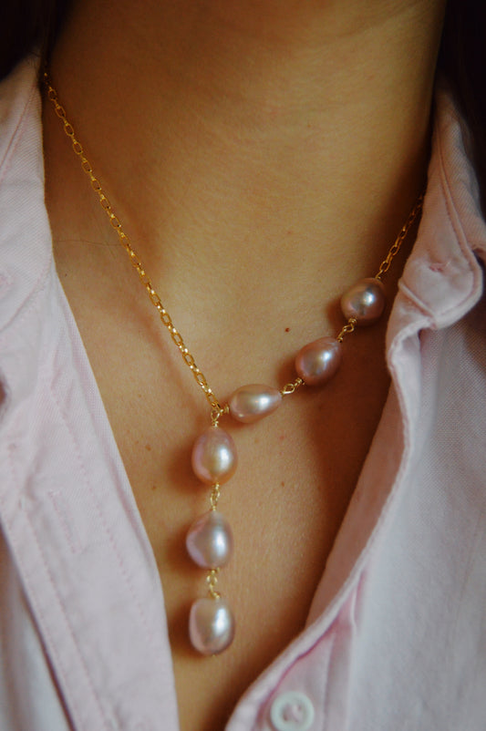 A close-up of a person wearing the Champagne Pearl Lariat—a handcrafted 14k gold-filled chain necklace with six irregularly shaped cultured freshwater pearls—paired with a light pink collared shirt.