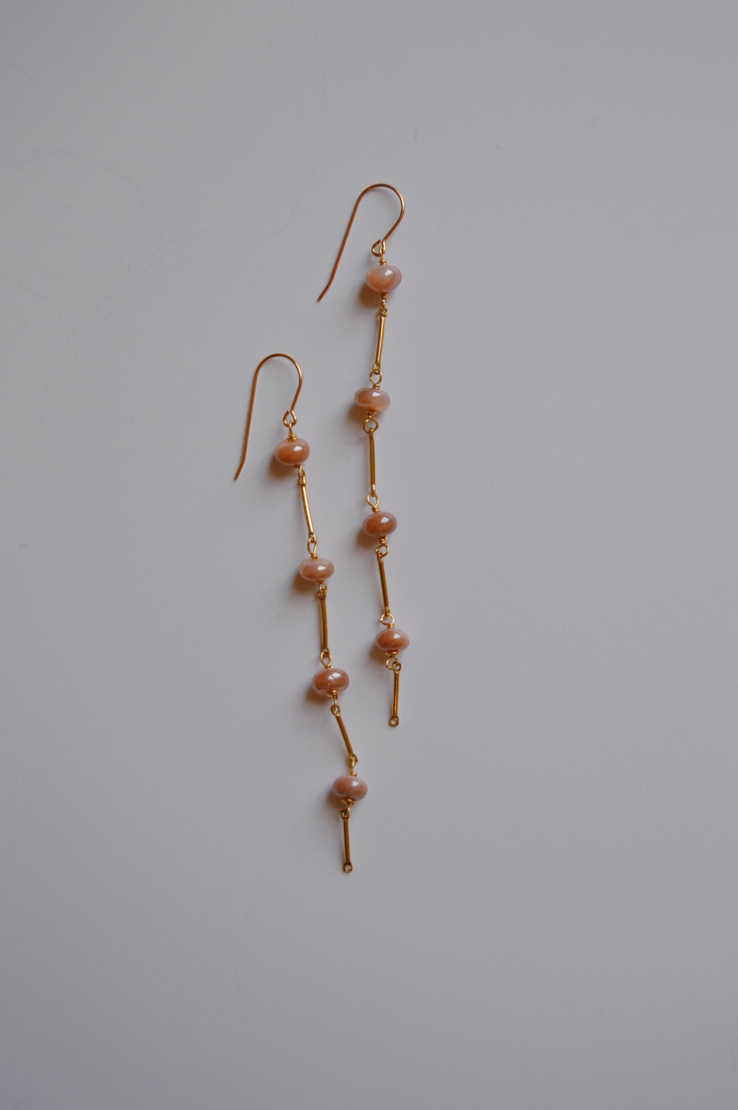 The Moonstone Dot Drops are elegant, handcrafted gold dangle earrings featuring pink pearls spaced along thin gold bars, shown on a plain white background.