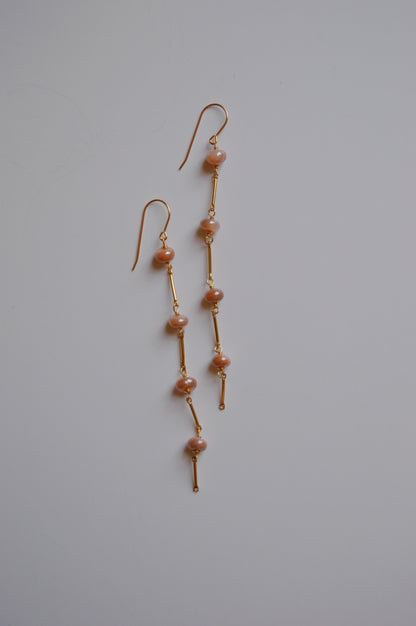 The Moonstone Dot Drops are elegant, handcrafted gold dangle earrings featuring pink pearls spaced along thin gold bars, shown on a plain white background.