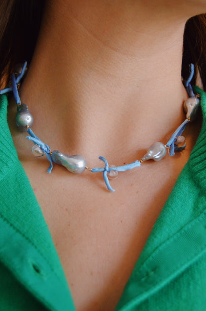 A close-up of a person wearing the Silk and Pearl Layer- Periwinkle necklace—irregular silver freshwater pearls on silk with a blue ribbon—paired with a green collared shirt.