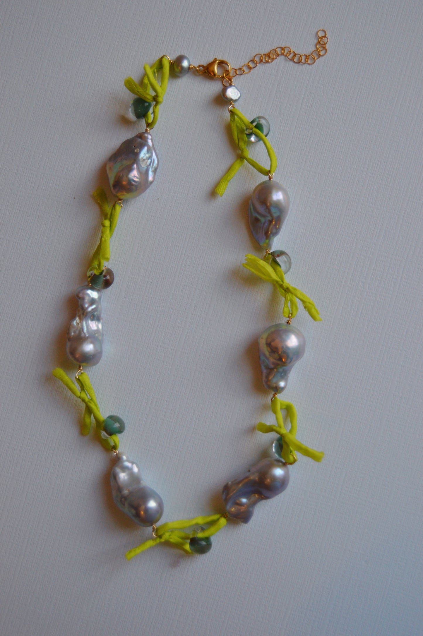 The Silk and Pearl Layer- Seafoam & Lime is a silk necklace with large, irregular freshwater pearls, small green beads, yellow fabric knot ties, and a gold adjustable clasp, shown on a light background.
