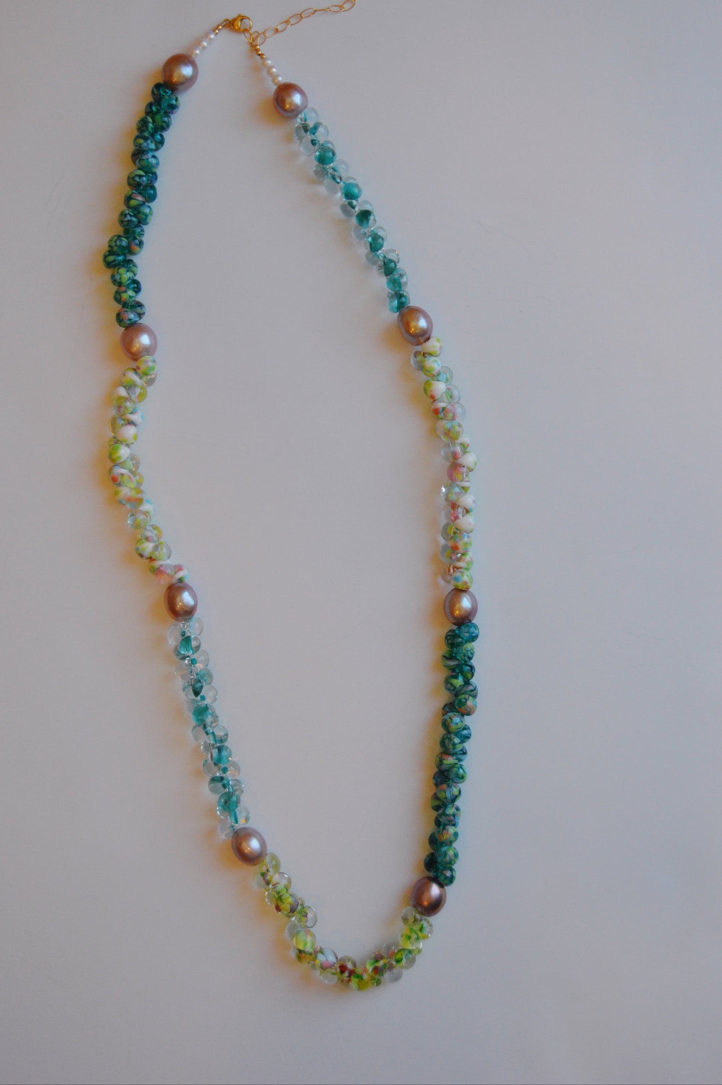 The Long Bubble Glass and Pearl Necklace features gradient beads from dark teal to pale yellow-green, accented with silver pearls, cultured freshwater pearls, and a 14k gold-filled clasp, displayed in an oval on a white background.