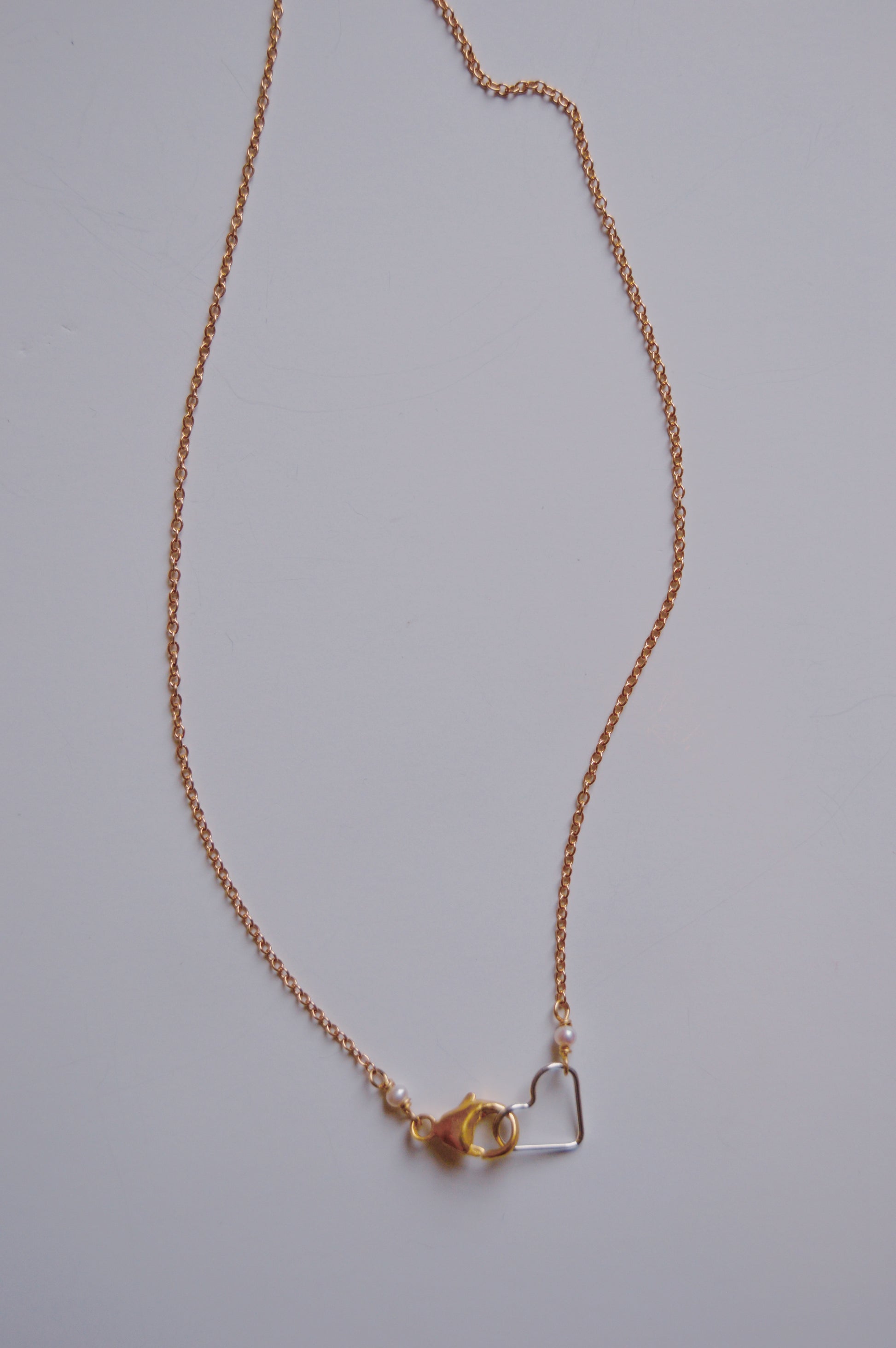 The Clasp in Front Layer necklace features a delicate 16" oxidized sterling silver chain with a lobster clasp and a small 14K gold-filled heart pendant, shown against a plain white background.