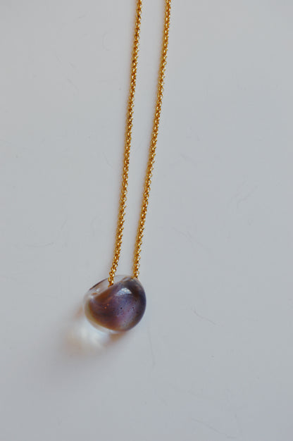 The Grand Bubble Single - Jupiter features a delicate gold filled chain with a smooth, oval, translucent pendant in purple and clear hues, shown on a white background.