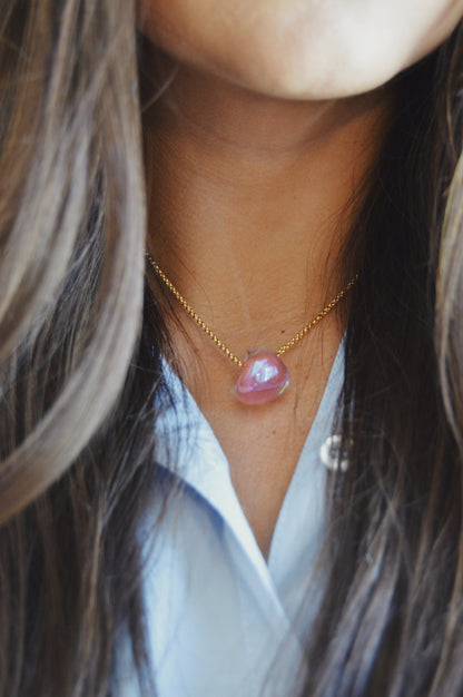 A close-up of a person with long brown hair wearing the Grand Bubble Single - Shimmer Pink, a 14k gold filled chain necklace with a pink gemstone pendant, paired with a light blue collared shirt.